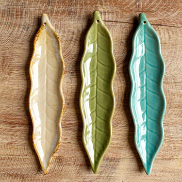 Three leaf-shaped ceramic plates in beige, green, and blue on a wooden surface