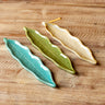 Three ceramic leaf-shaped dishes in teal, green, and beige on a wooden surface.